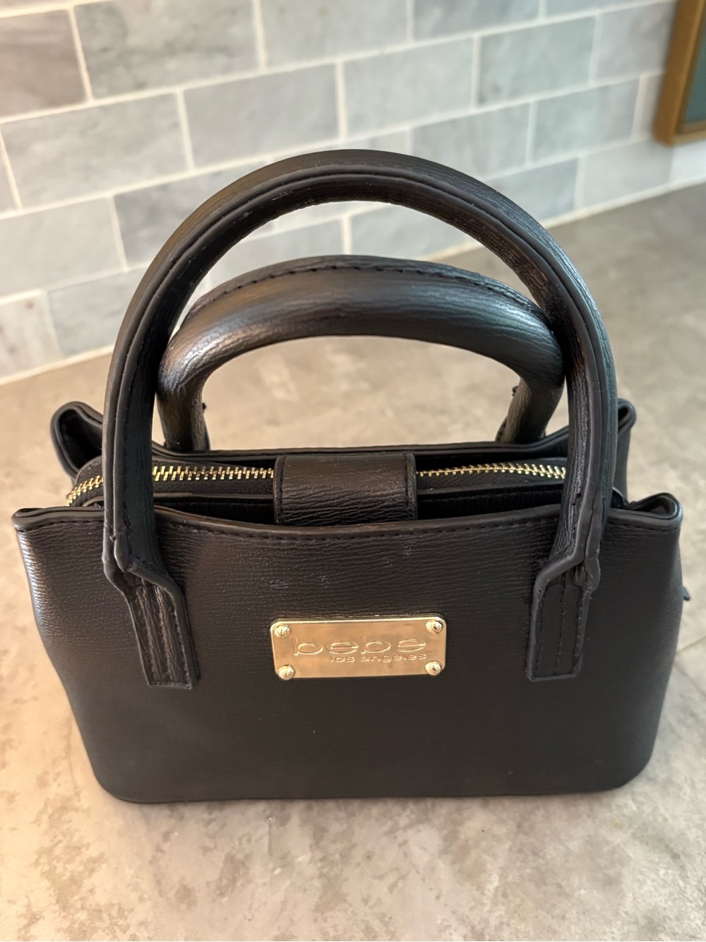 Bebe satchel features a prominent gold-toned logo plate and removable strap